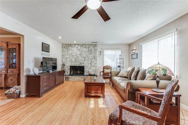 living room with light wood-type flooring, ceiling fan, a textured ceiling, and a fireplace