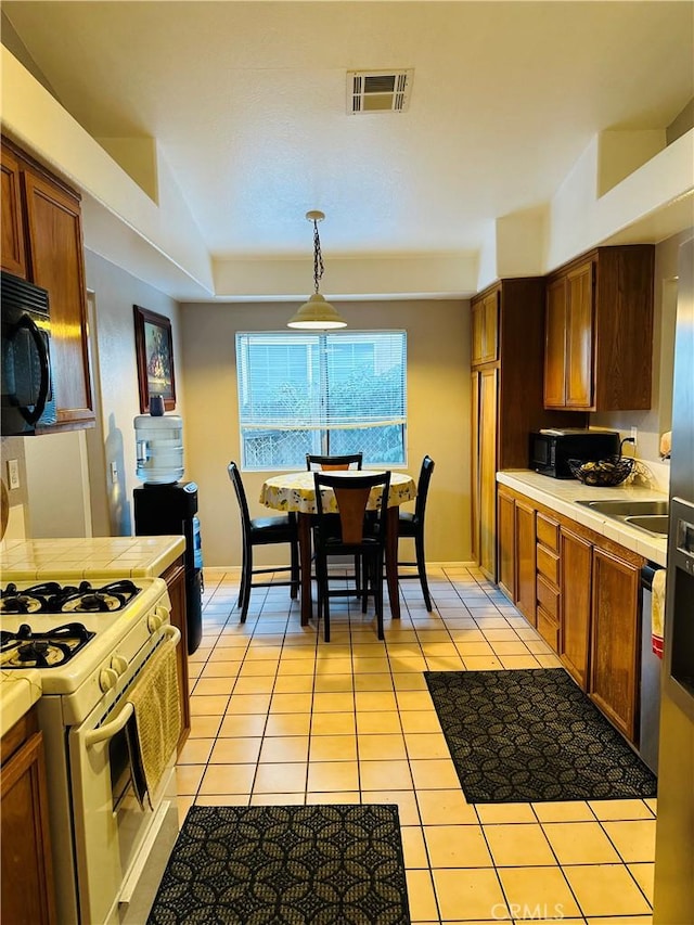 kitchen with dishwasher, light tile patterned floors, hanging light fixtures, and white gas range oven