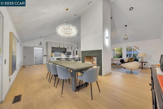 dining room featuring a notable chandelier, light hardwood / wood-style floors, and high vaulted ceiling