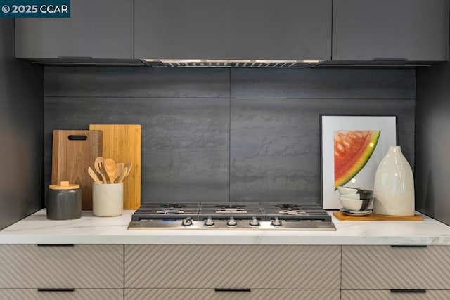 interior details with decorative backsplash, light stone countertops, and stainless steel gas cooktop