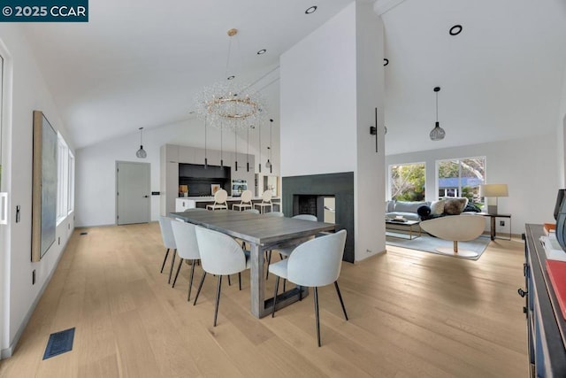 dining room featuring high vaulted ceiling, a multi sided fireplace, a chandelier, and light wood-type flooring