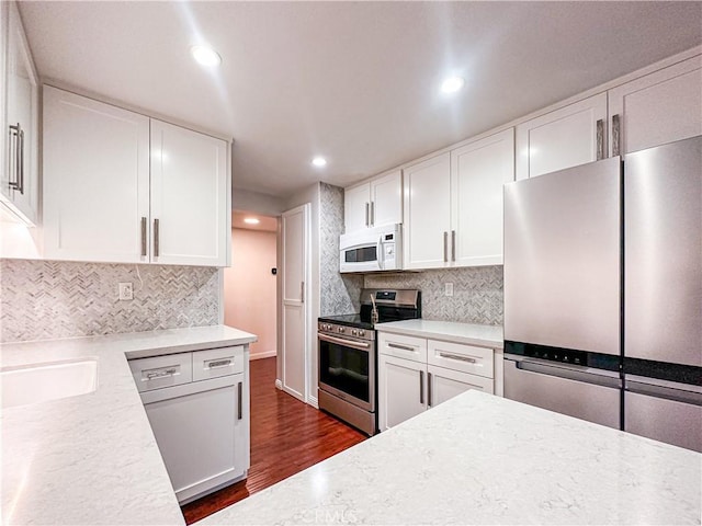 kitchen featuring decorative backsplash, appliances with stainless steel finishes, dark hardwood / wood-style flooring, sink, and white cabinetry