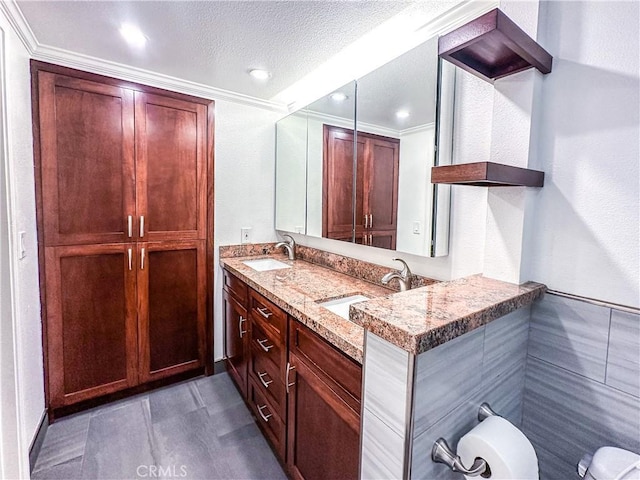 full bath featuring double vanity, crown molding, a textured ceiling, and a sink