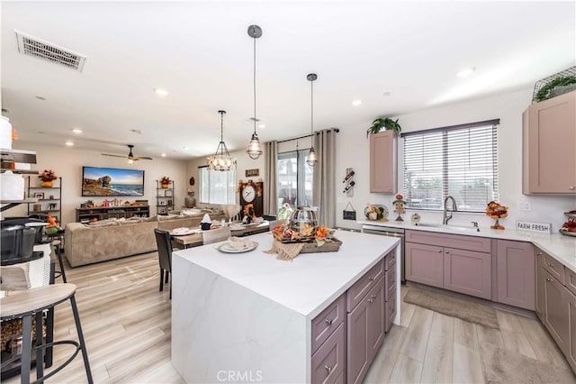 kitchen featuring pendant lighting, ceiling fan with notable chandelier, sink, light wood-type flooring, and a kitchen island