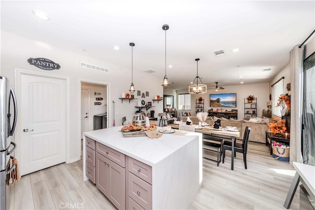 kitchen with stainless steel fridge, light wood-type flooring, ceiling fan, pendant lighting, and a kitchen island