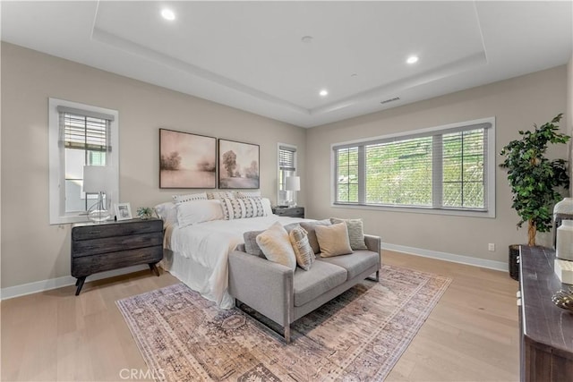 bedroom featuring a raised ceiling, multiple windows, and light hardwood / wood-style floors