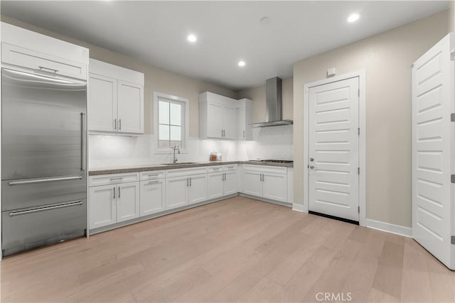 kitchen featuring wall chimney exhaust hood, white cabinetry, light hardwood / wood-style flooring, and built in refrigerator