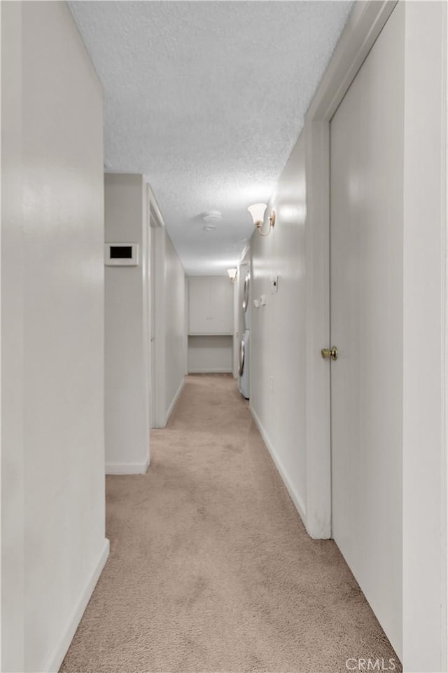 hallway featuring light carpet, a textured ceiling, and washer / dryer