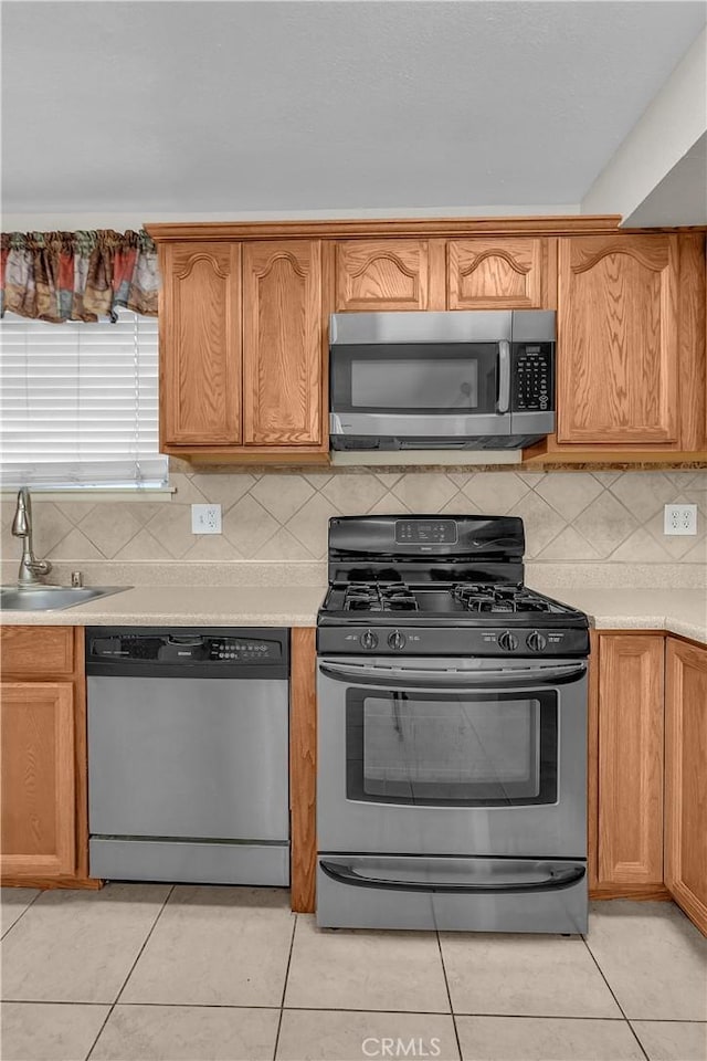 kitchen featuring decorative backsplash, sink, light tile patterned floors, and appliances with stainless steel finishes