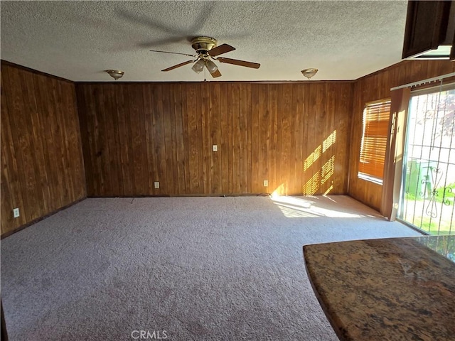 carpeted spare room featuring a textured ceiling, ceiling fan, and wooden walls