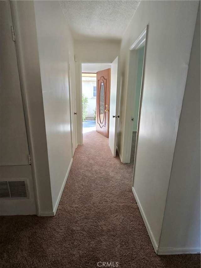 hall featuring a textured ceiling, carpet, visible vents, and baseboards