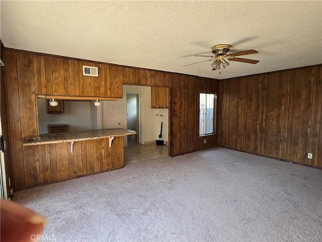 kitchen featuring carpet, brown cabinets, visible vents, a textured ceiling, and a peninsula