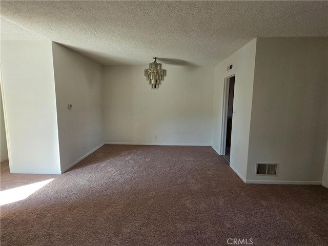 carpeted spare room featuring baseboards, a notable chandelier, visible vents, and a textured ceiling