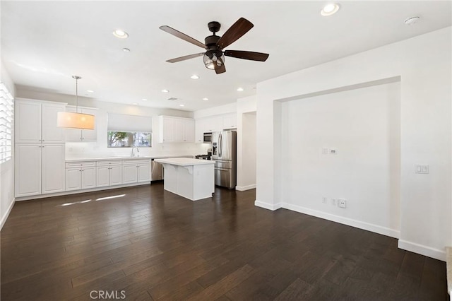 kitchen with pendant lighting, a center island, dark wood-type flooring, white cabinetry, and stainless steel appliances