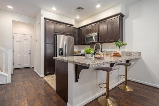 kitchen featuring light hardwood / wood-style floors, a breakfast bar, dark brown cabinetry, appliances with stainless steel finishes, and sink