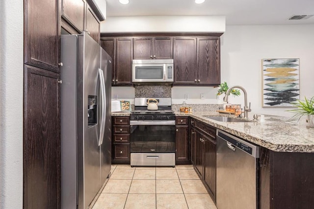 kitchen featuring stainless steel appliances, kitchen peninsula, light tile patterned floors, sink, and dark brown cabinets