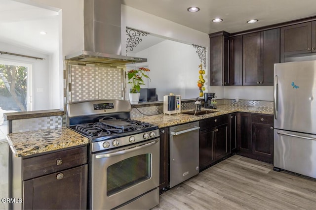 kitchen with light stone counters, wall chimney range hood, light wood-type flooring, and appliances with stainless steel finishes