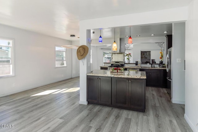 kitchen with light stone countertops, kitchen peninsula, pendant lighting, light wood-type flooring, and appliances with stainless steel finishes