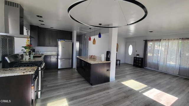 kitchen featuring light stone counters, stainless steel appliances, exhaust hood, and light hardwood / wood-style flooring