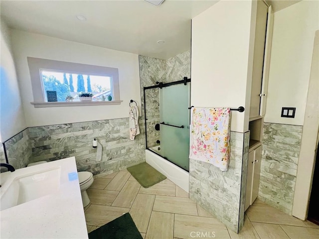 full bathroom featuring vanity, toilet, enclosed tub / shower combo, and tile walls