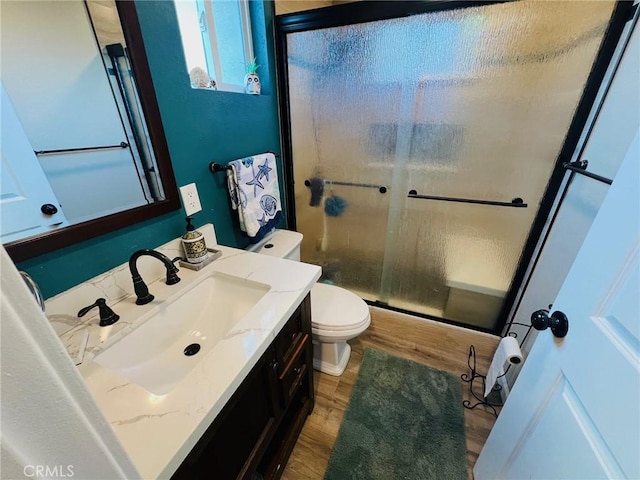 bathroom featuring wood-type flooring, vanity, toilet, and a shower with shower door