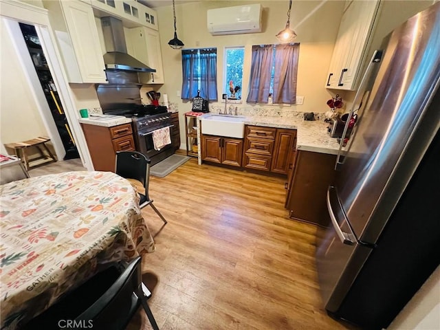 kitchen with sink, a wall mounted air conditioner, wall chimney range hood, decorative light fixtures, and appliances with stainless steel finishes