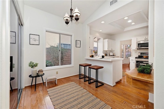 kitchen featuring light hardwood / wood-style flooring, kitchen peninsula, a breakfast bar area, white cabinets, and appliances with stainless steel finishes