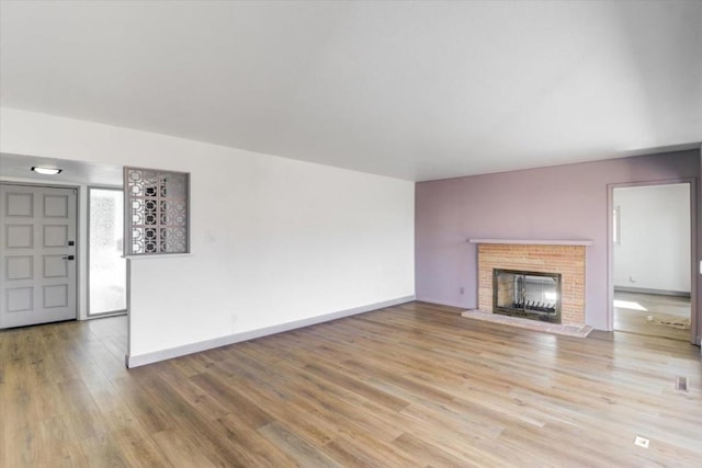 unfurnished living room with a brick fireplace and light wood-type flooring