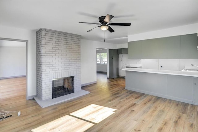 unfurnished living room featuring ceiling fan, light hardwood / wood-style floors, a brick fireplace, and sink