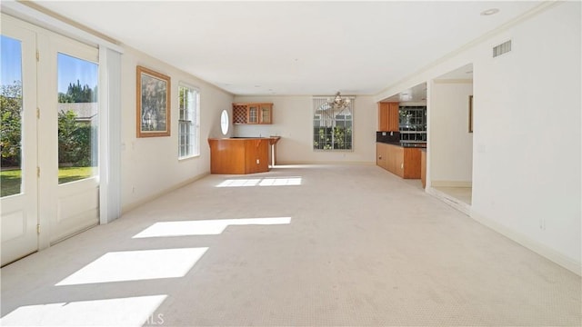 unfurnished living room featuring light carpet, plenty of natural light, a notable chandelier, and ornamental molding