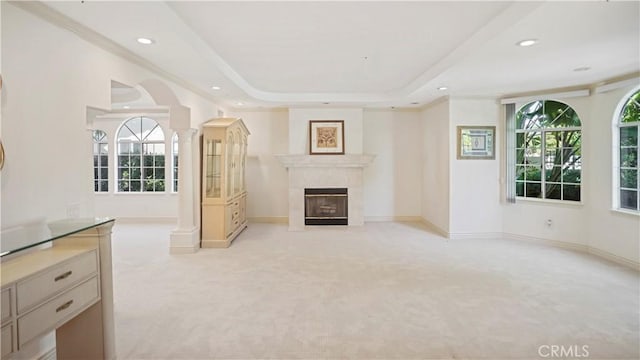 unfurnished living room with a tray ceiling, ornate columns, a wealth of natural light, and light carpet