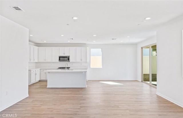 kitchen with a sink, visible vents, open floor plan, light wood finished floors, and stainless steel microwave