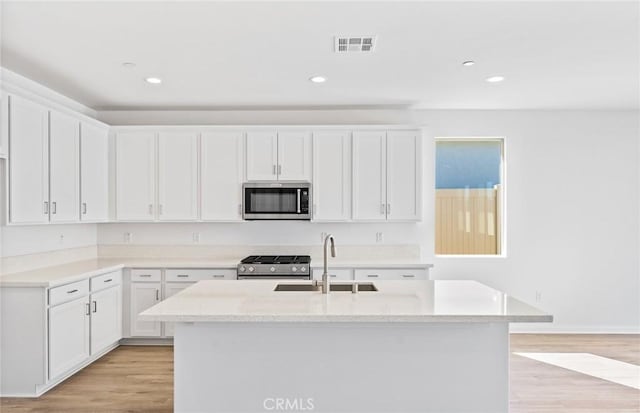 kitchen featuring light wood-type flooring, appliances with stainless steel finishes, white cabinets, and a sink