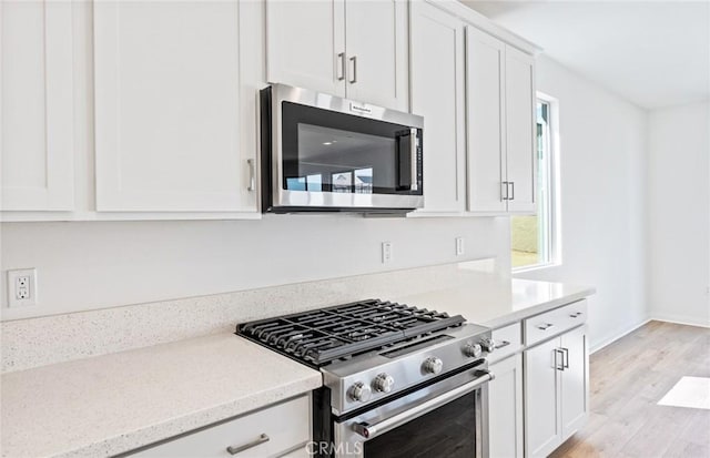 kitchen featuring baseboards, white cabinets, light wood-style flooring, appliances with stainless steel finishes, and light stone counters