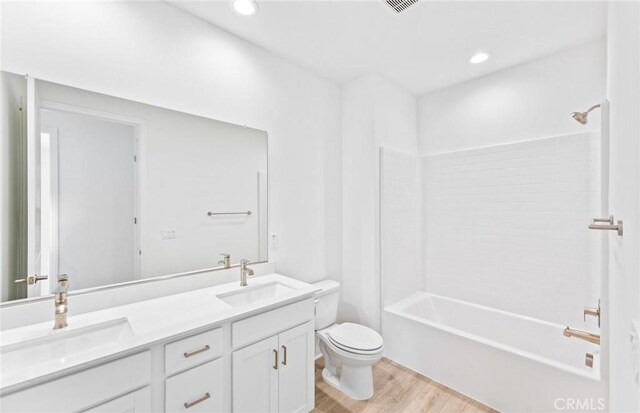 full bath with double vanity, a sink, toilet, and wood finished floors