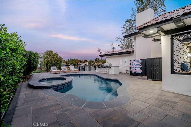 pool at dusk featuring an in ground hot tub and a patio