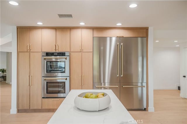 kitchen featuring light hardwood / wood-style floors, light stone counters, light brown cabinetry, and appliances with stainless steel finishes