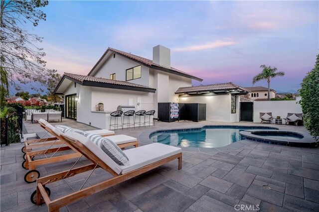 back house at dusk featuring a pool with hot tub, a patio area, and exterior bar