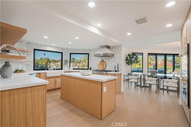 kitchen with a kitchen island, light wood-type flooring, light brown cabinets, and range hood