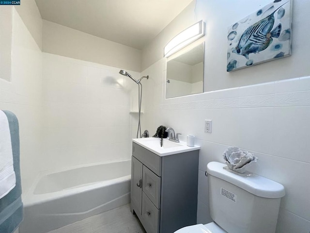 full bathroom featuring tiled shower / bath, vanity, tile walls, and toilet