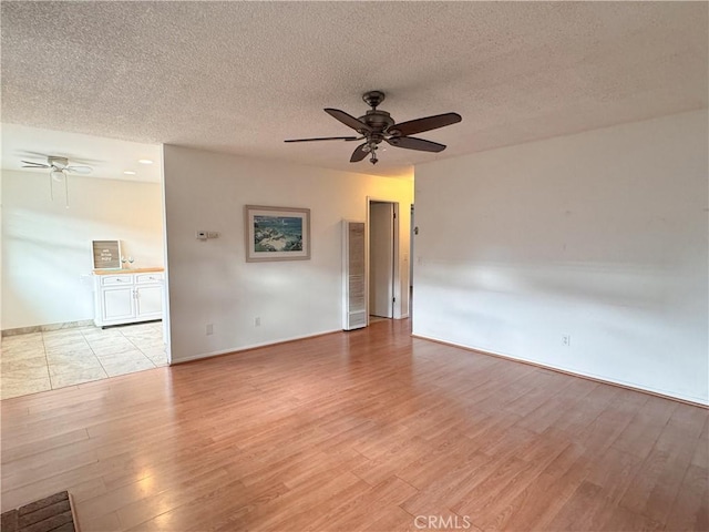 unfurnished room with ceiling fan, light wood-type flooring, and a textured ceiling