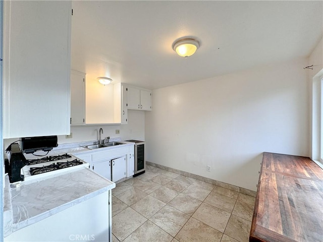 kitchen featuring gas stove, sink, white cabinets, and beverage cooler