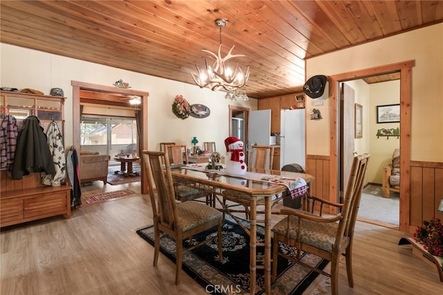 dining area with hardwood / wood-style floors, a notable chandelier, wood ceiling, and wooden walls