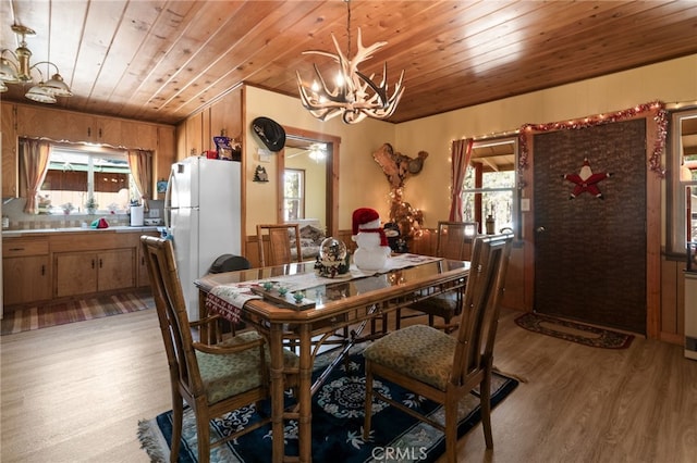 dining room with ceiling fan with notable chandelier, wood ceiling, a wealth of natural light, and light hardwood / wood-style flooring