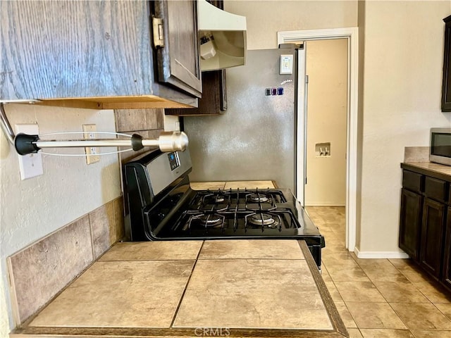 kitchen with dark brown cabinets, light tile patterned floors, and black gas range