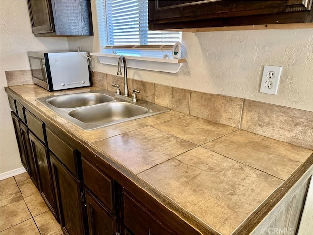 kitchen featuring dark brown cabinets, tile countertops, light tile patterned floors, and sink