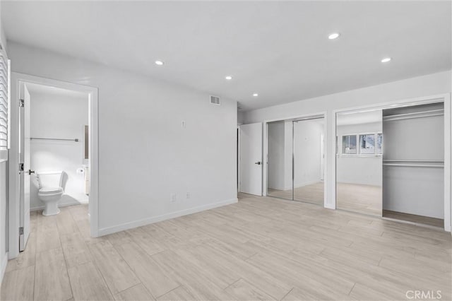 unfurnished bedroom featuring connected bathroom, light hardwood / wood-style floors, and two closets