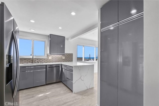 kitchen featuring kitchen peninsula, light stone counters, gray cabinetry, stainless steel appliances, and light hardwood / wood-style floors