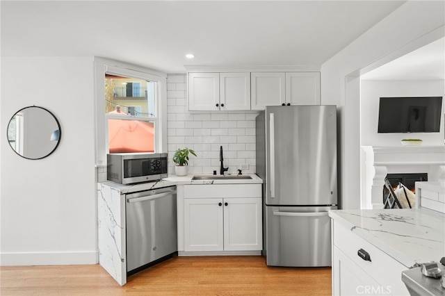 kitchen with appliances with stainless steel finishes, light hardwood / wood-style flooring, white cabinetry, and sink