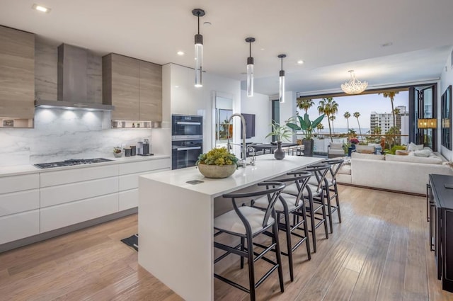 kitchen featuring light hardwood / wood-style floors, a kitchen bar, a center island with sink, decorative light fixtures, and wall chimney range hood